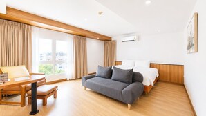 A hotel room with a bed, a sofa, a dining table, and a window with curtains. - Cozy Don Mueang Hotel (Bangkok)