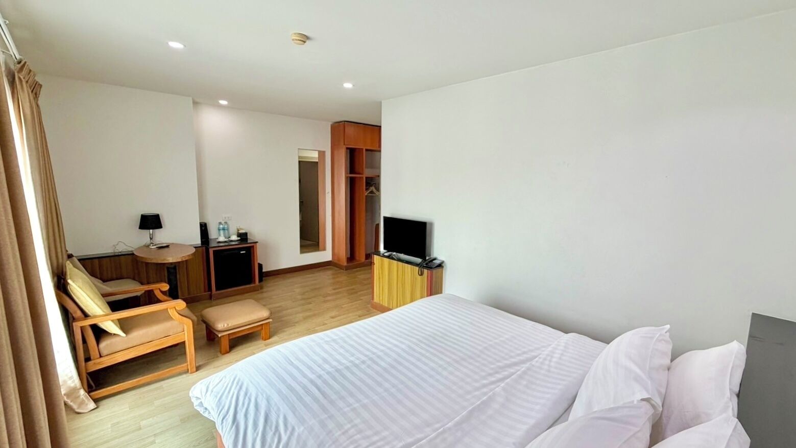 A hotel room with a bed, a desk with a chair, a TV, and a wardrobe.