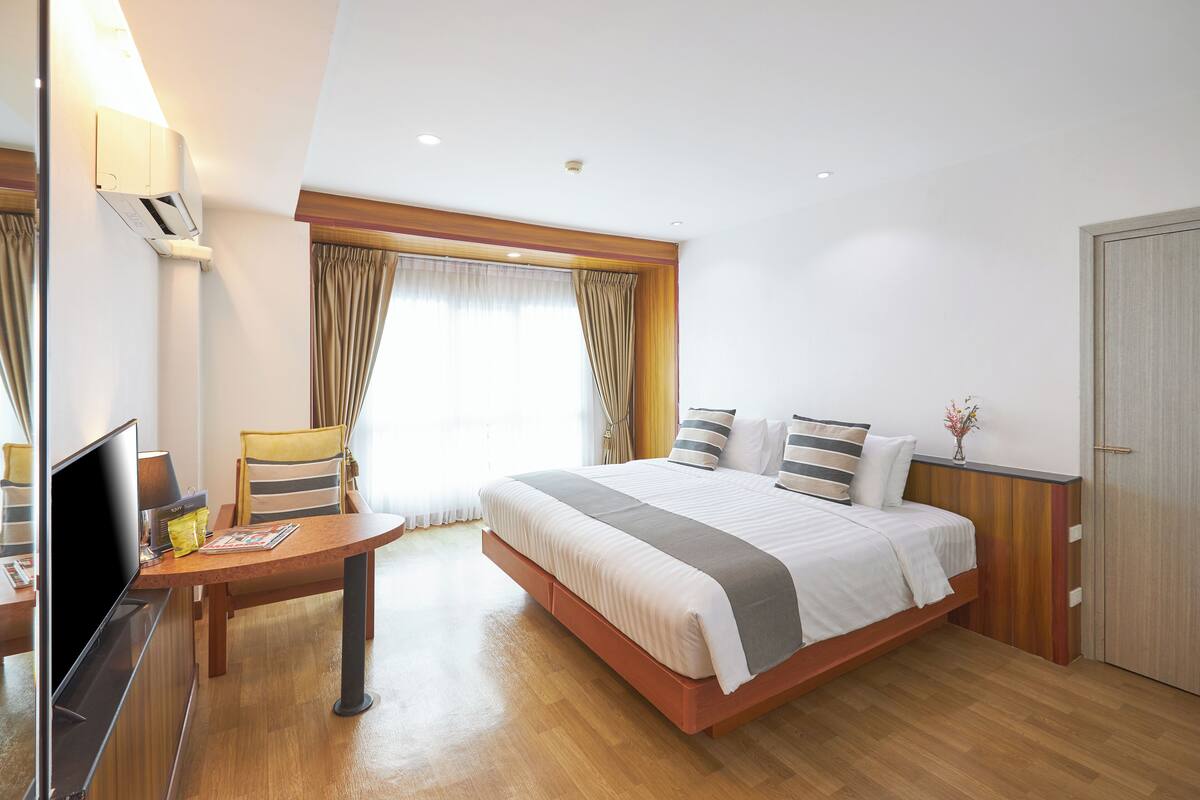 A hotel room with a bed, a desk with a TV, and a window with curtains.