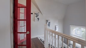 Un escalier avec une porte rouge, des rampes blanches et deux œuvres d’art accrochées au mur.