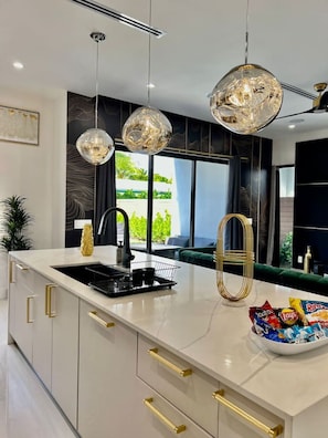 Una cocina moderna con una isla central, luces colgantes y vistas al exterior.