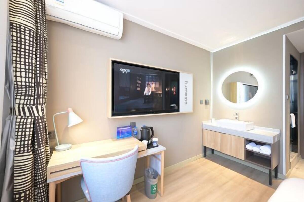 A hotel room with a TV, desk, chair, and a bathroom with a mirror and sink.