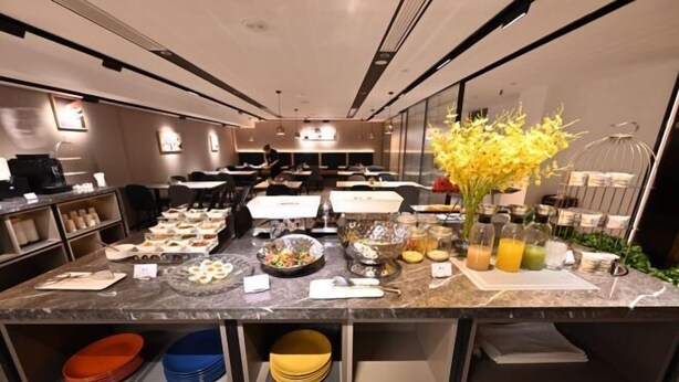 A modern hotel breakfast area with a marble counter, various breakfast items, and a vase of yellow flowers. - Homeinn · neo (Beijing Ping'anli Subway Station) (Beijing)