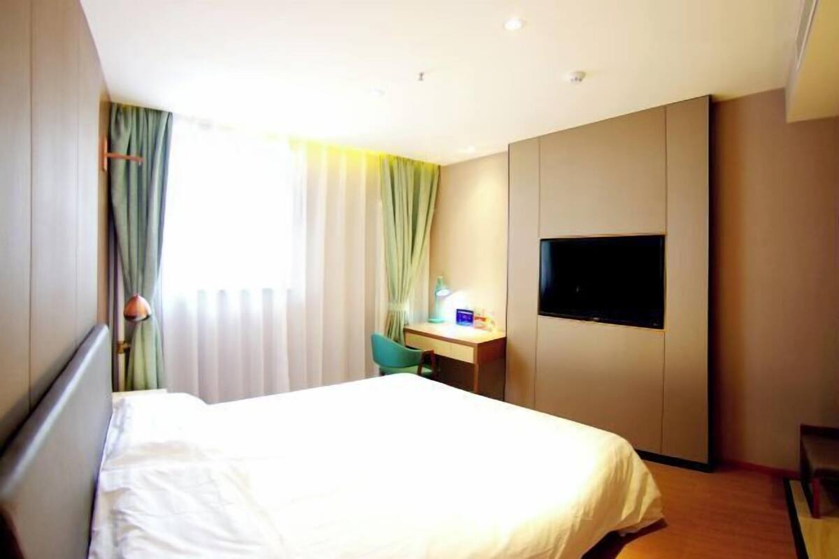 A hotel room with a bed, a desk, a chair, a TV, and a window with curtains.