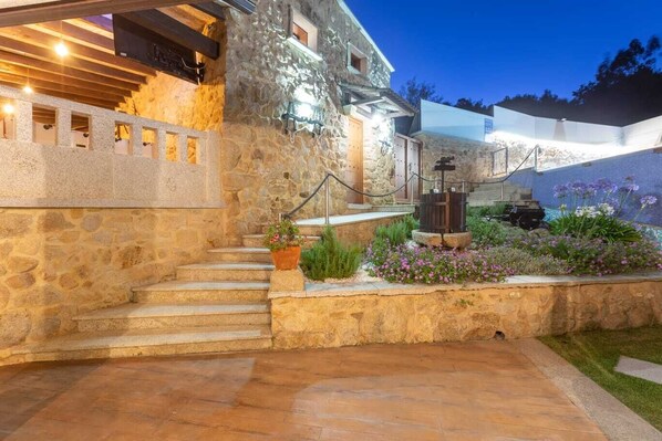 A stone building with a stone staircase leading to a door, surrounded by a garden with flowers and a barbecue area. - Villa Alma (O Sartal)