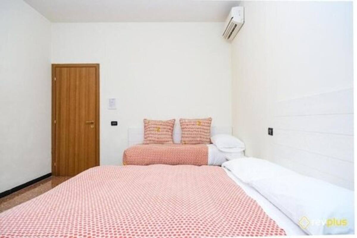 Une chambre avec une porte en bois, un lit recouvert d’une couvre-lit à motifs et une table de chevet blanche.