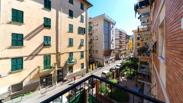 A narrow street with buildings on either side, balconies with laundry, and a clear sky.