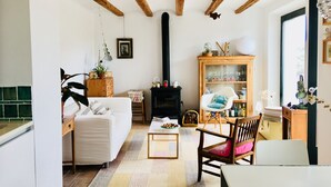 Una sala de estar acogedora con chimenea, vigas de madera, un sofá, una mesa de centro y un aparador con cristalería.