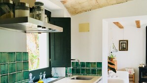 Una cocina con estufa moderna, lavamanos y salpicadero con azulejos verdes. Hay una zona de comedor con un sofá blanco y una mesa pequeña.
