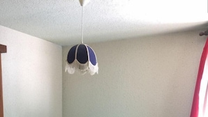A small, simple room with a single bed, a hanging light fixture, and a window with curtains.