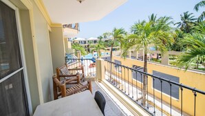 A balcony with a table and chairs, overlooking a pool and palm trees. - Garden Condos 40, 1br Apt In Sosua Strip! Guest Ok (Sosúa)