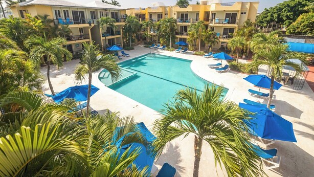 A hotel with a swimming pool surrounded by palm trees and blue umbrellas. - Garden Condos 40, 1br Apt In Sosua Strip! Guest Ok (Sosúa)
