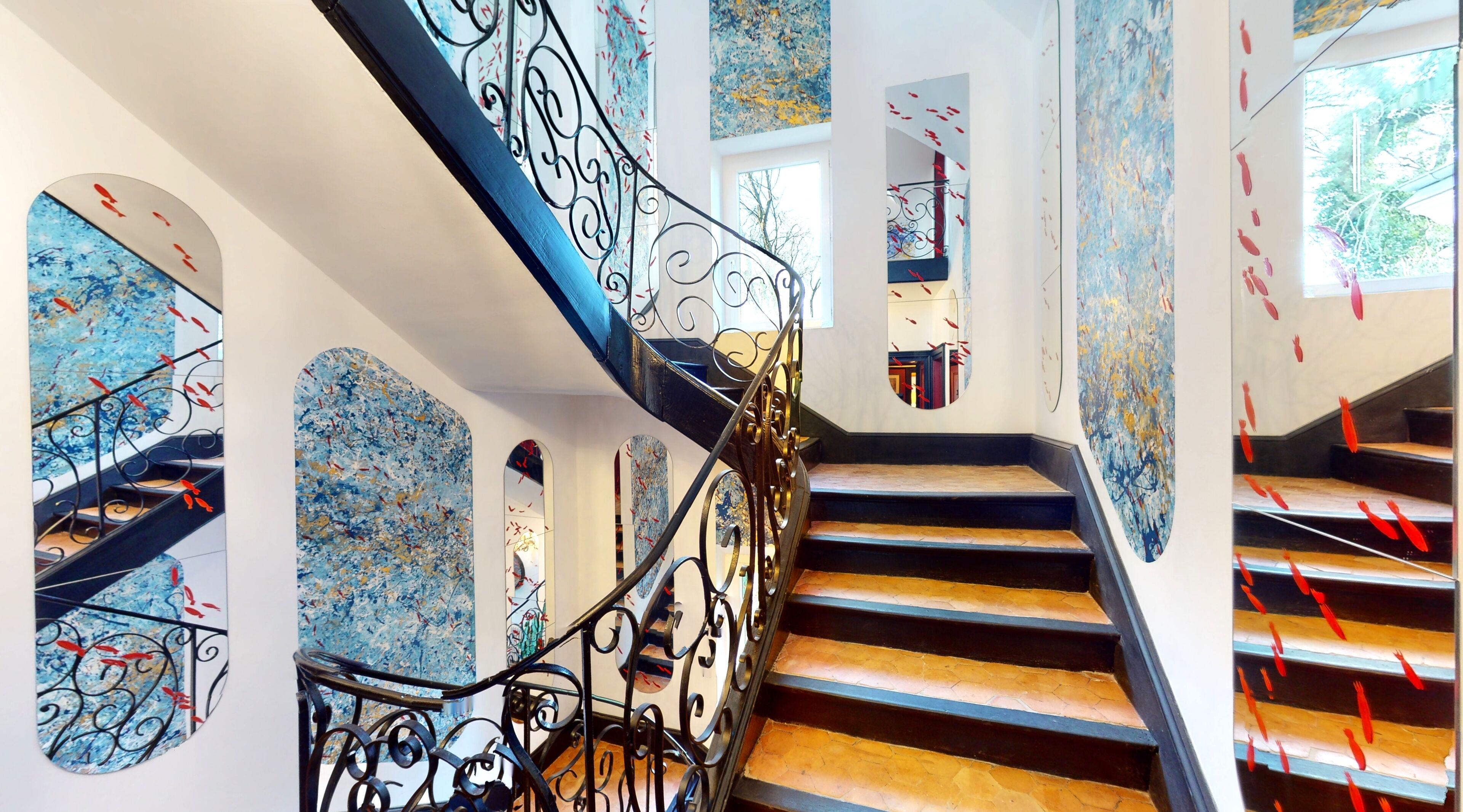 Un escalier en colimaçon orné de rampes noires travaillées et agrémenté d’œuvres d’art murales abstraites aux tons bleus.