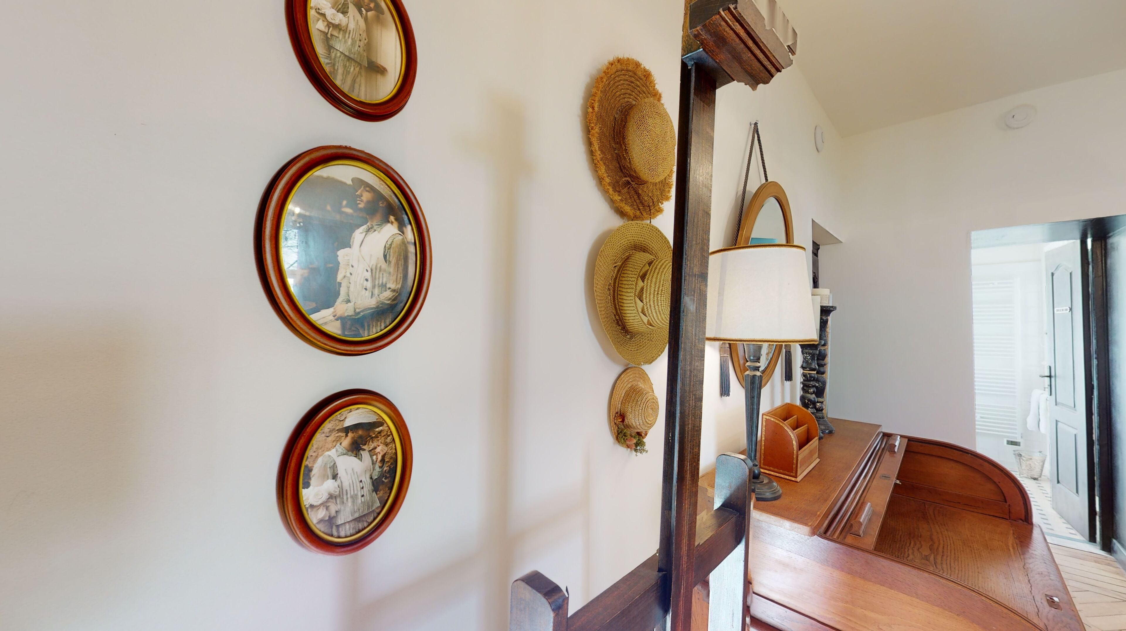 A hallway with framed pictures on the wall, a lamp, and a wooden bench.
