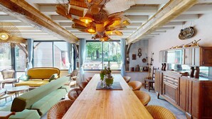 Una habitación amplia con una mesa de comedor de madera, muebles de mimbre y un ventanal que ofrece vistas al exterior.