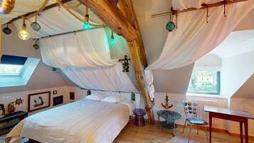 Een gezellige slaapkamer met een groot bed, een bureau en een stoel. Er zijn hanglampen en een raam met uitzicht.