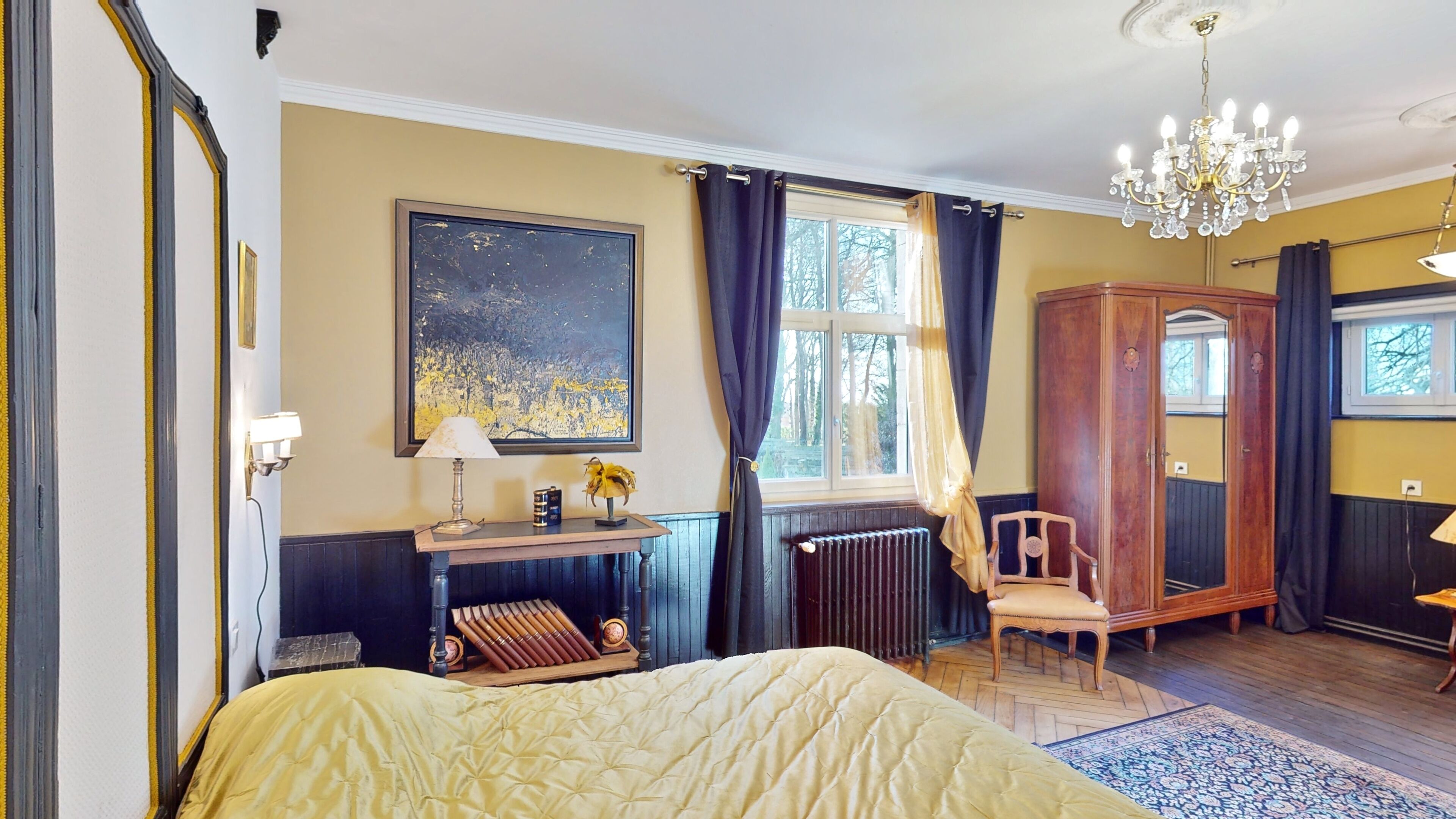 A bedroom with a large bed, a wooden wardrobe, a nightstand with a lamp, a painting on the wall, and a window with curtains.