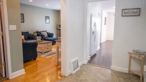 Un salon moderne avec un canapé bleu, une table basse et une petite table d’appoint. Une porte donne accès à une autre pièce et un panneau indiquant « BIENVENUE » est accroché au mur.
