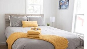 Une chambre à coucher avec un cadre de lit en bois, une couvre-lit grise et jaune, et un plaid jaune.