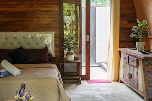 Un dormitorio con cama, cabecera de madera, planta en maceta, aparador de madera y puerta que da al exterior.