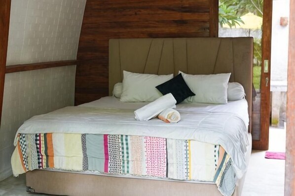 A bed with a patterned bedspread, a rolled towel, and pillows.