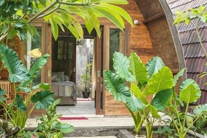 A wooden house with a large sliding door, a bed, and a small waterfall feature.