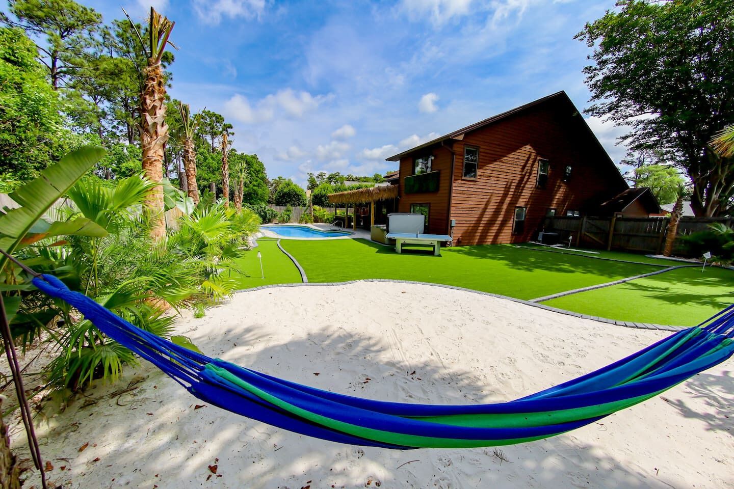 A house with a swimming pool, a hammock, and a well-maintained lawn.