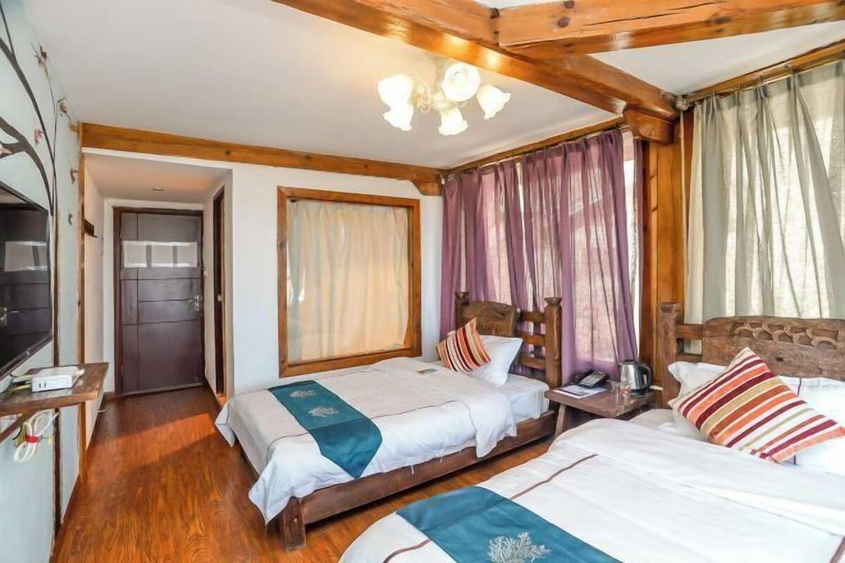 A hotel room with two beds, wooden beams, a ceiling light, a desk with a telephone, and a door leading to a bathroom.