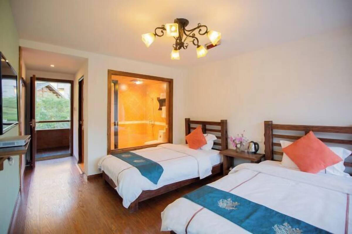 A hotel room with two beds, a wooden floor, a large window, and a chandelier.