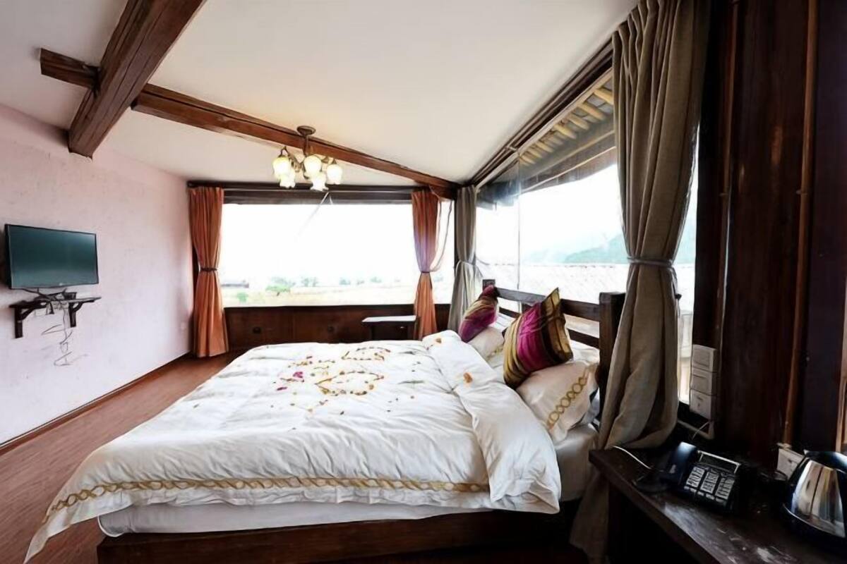 A bed with a white bedspread, a television on the wall, and a window with curtains.