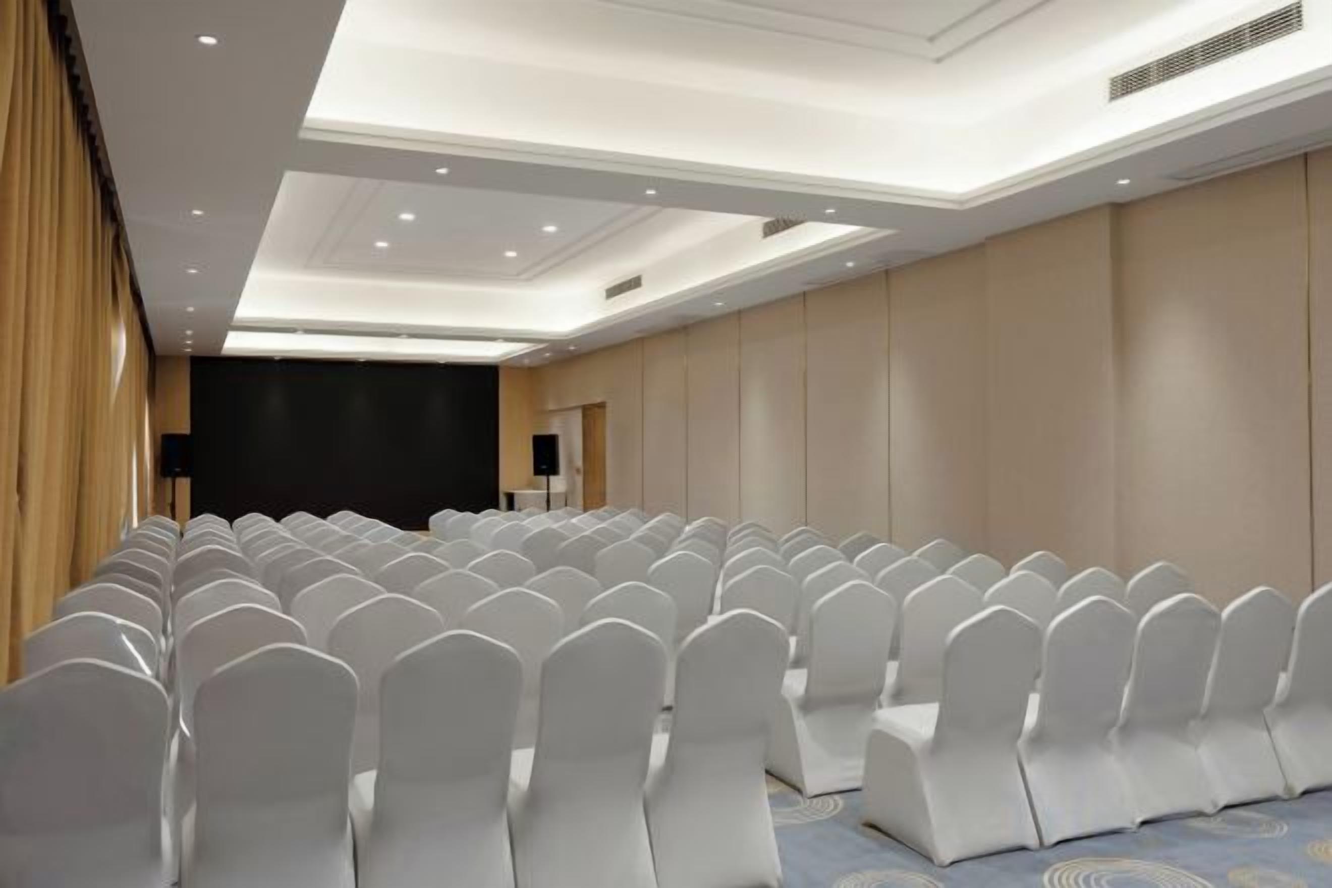 A conference room with rows of white chairs, a stage with a black backdrop, and a podium.