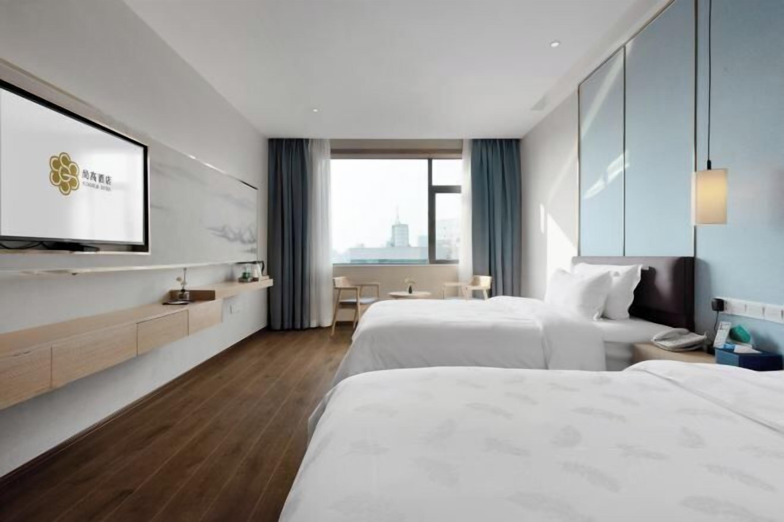 Habitación de hotel con dos camas, un televisor montado en la pared, un escritorio y una ventana con vista a la ciudad.