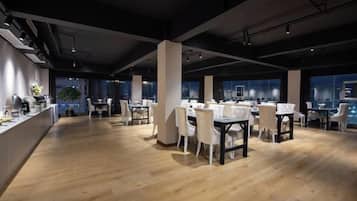 A spacious dining area with high ceilings and modern lighting, featuring multiple tables and chairs.