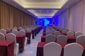 A conference room with rows of tables and chairs, a blue-lit stage, and a carpeted floor. - Shanggao Hotel (Chongqing)