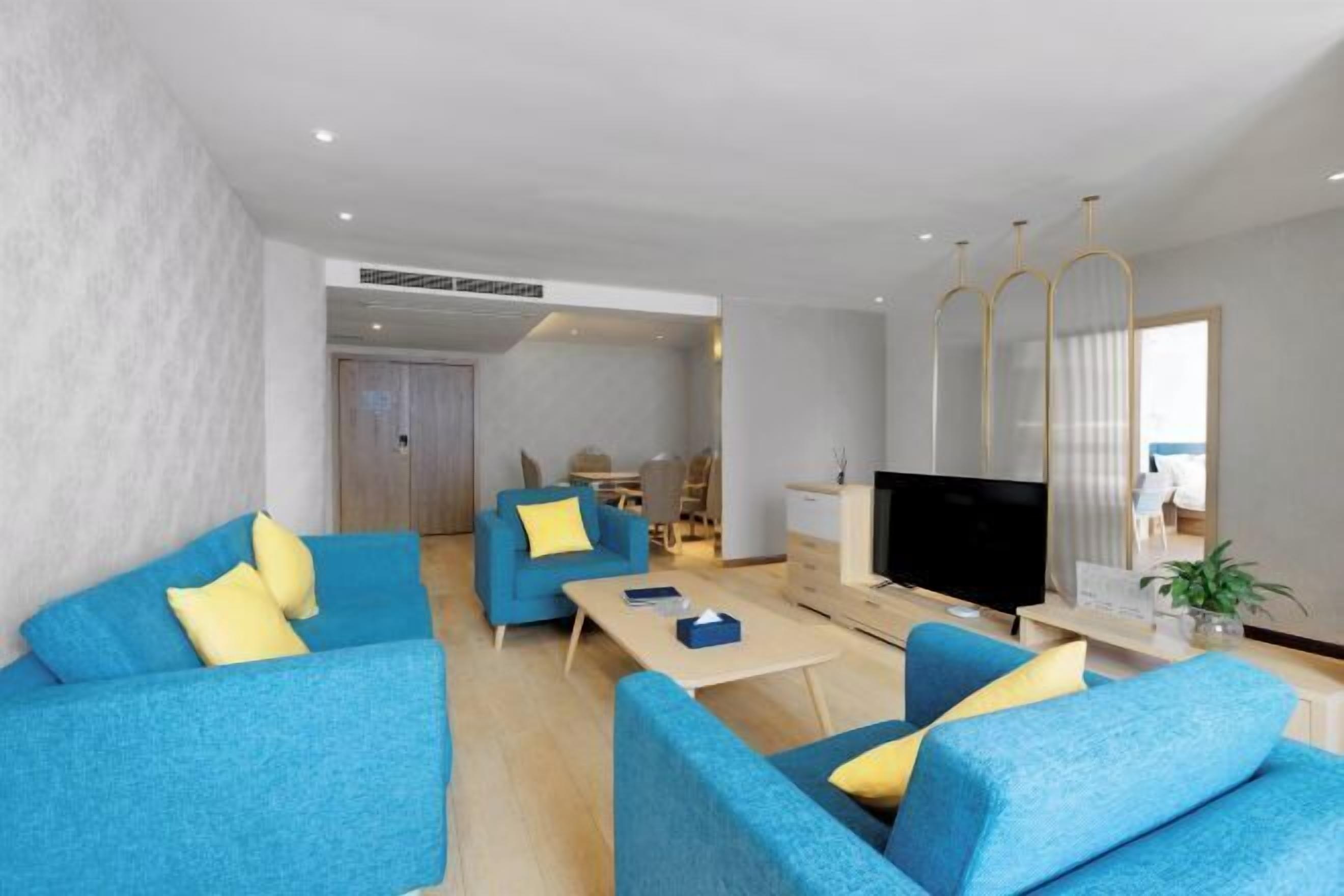 Un salon moderne avec des canapés bleus, un téléviseur à écran plat et un coin repas comprenant une table et des chaises.