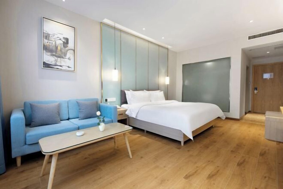 A modern hotel room with a bed, a sofa, a small table, and a wall-mounted artwork.
