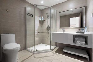A modern bathroom with a glass shower enclosure, a toilet, a sink with a mirror, and a shelf with towels. - Shanggao Hotel (Chongqing)