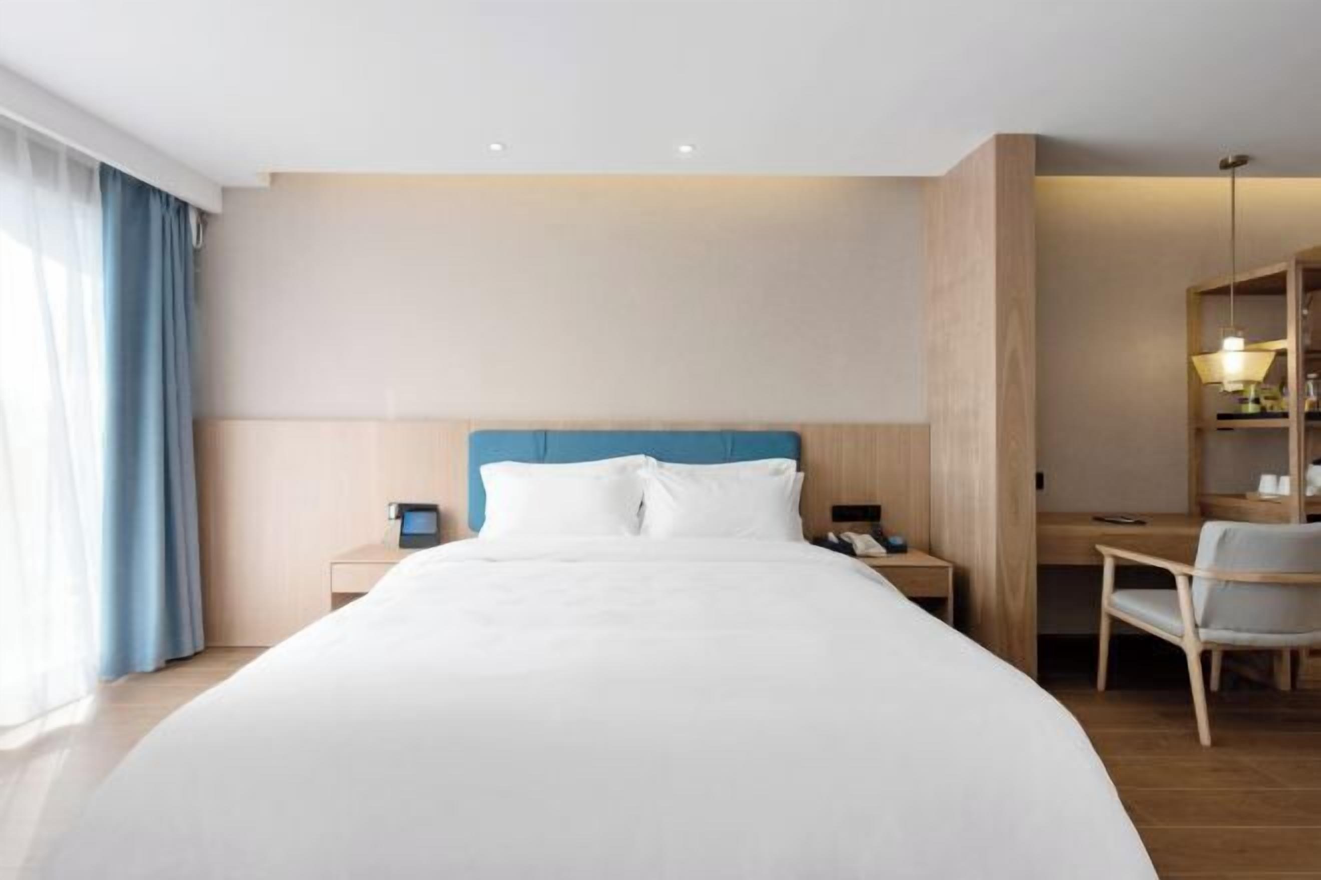 A hotel room with a bed, bedside tables, a desk, a chair, and a wardrobe.