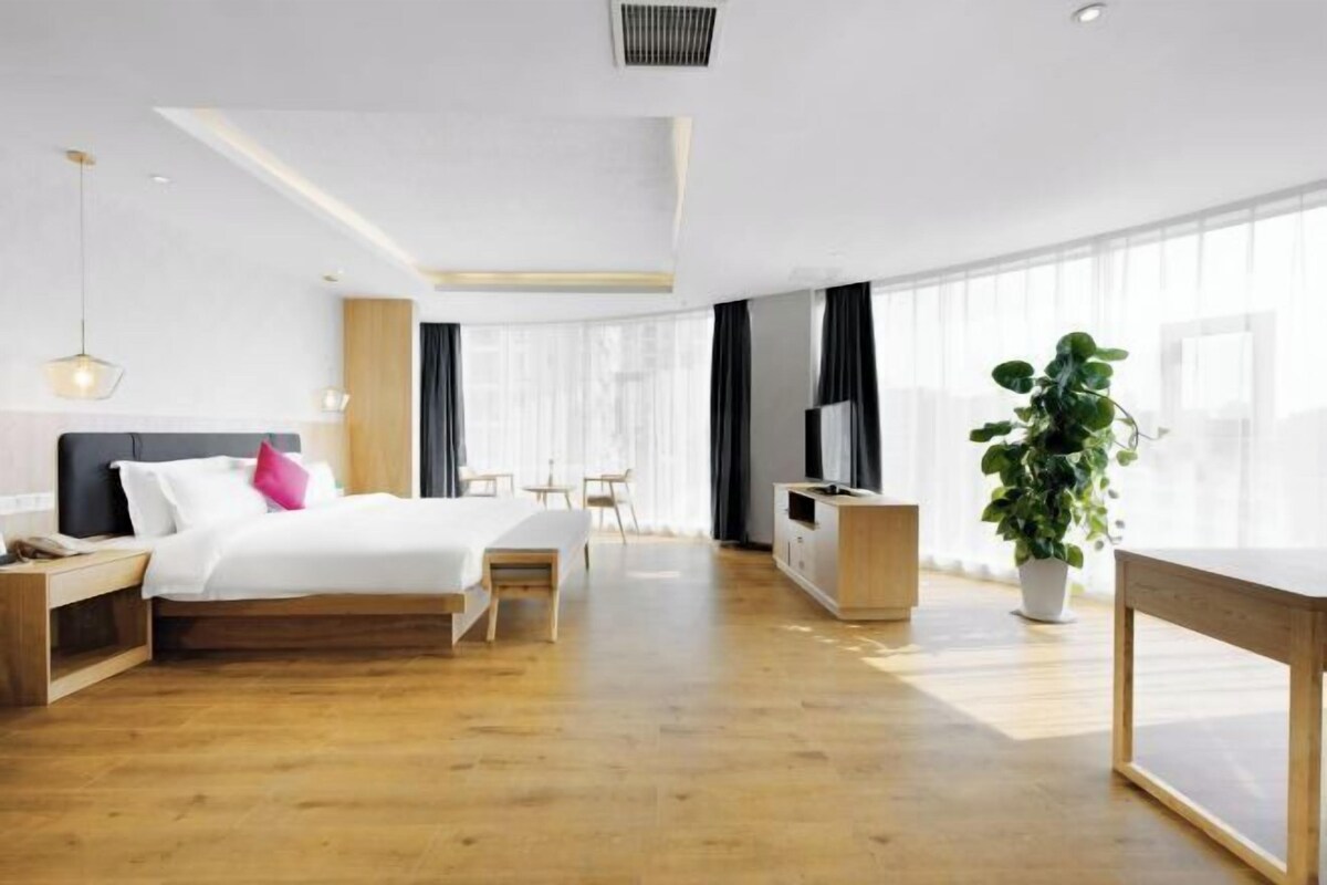 A modern hotel room with a bed, bedside table, TV, and a large window.