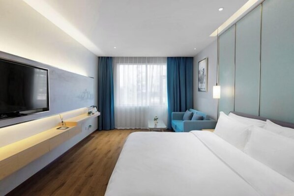 A modern hotel room with a large bed, a flat-screen TV, a sofa, a small table, and a window with curtains.