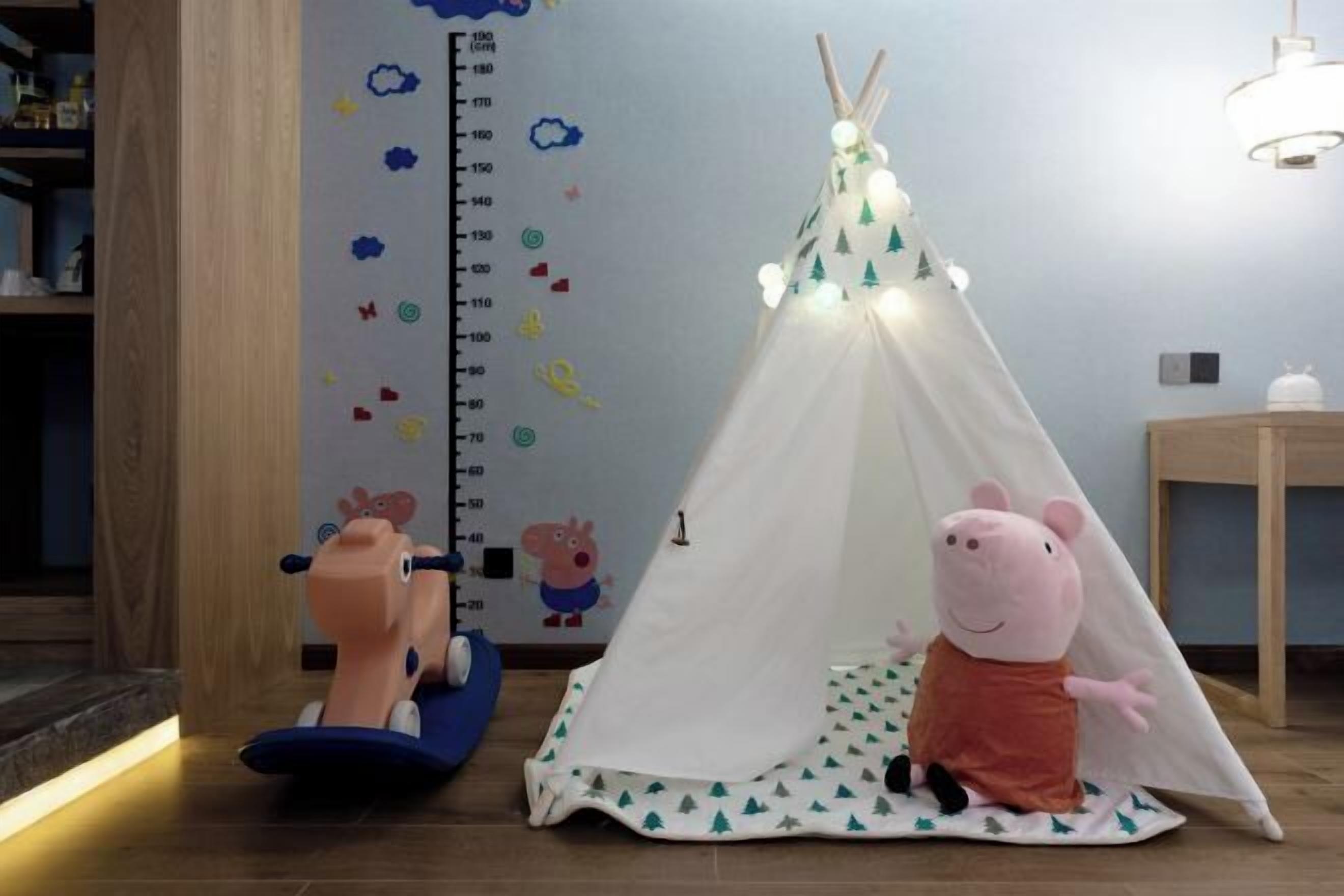 Un espace de jeux pour enfants avec une tente, un tableau pour mesurer la taille et une peluche de Peppa Pig.