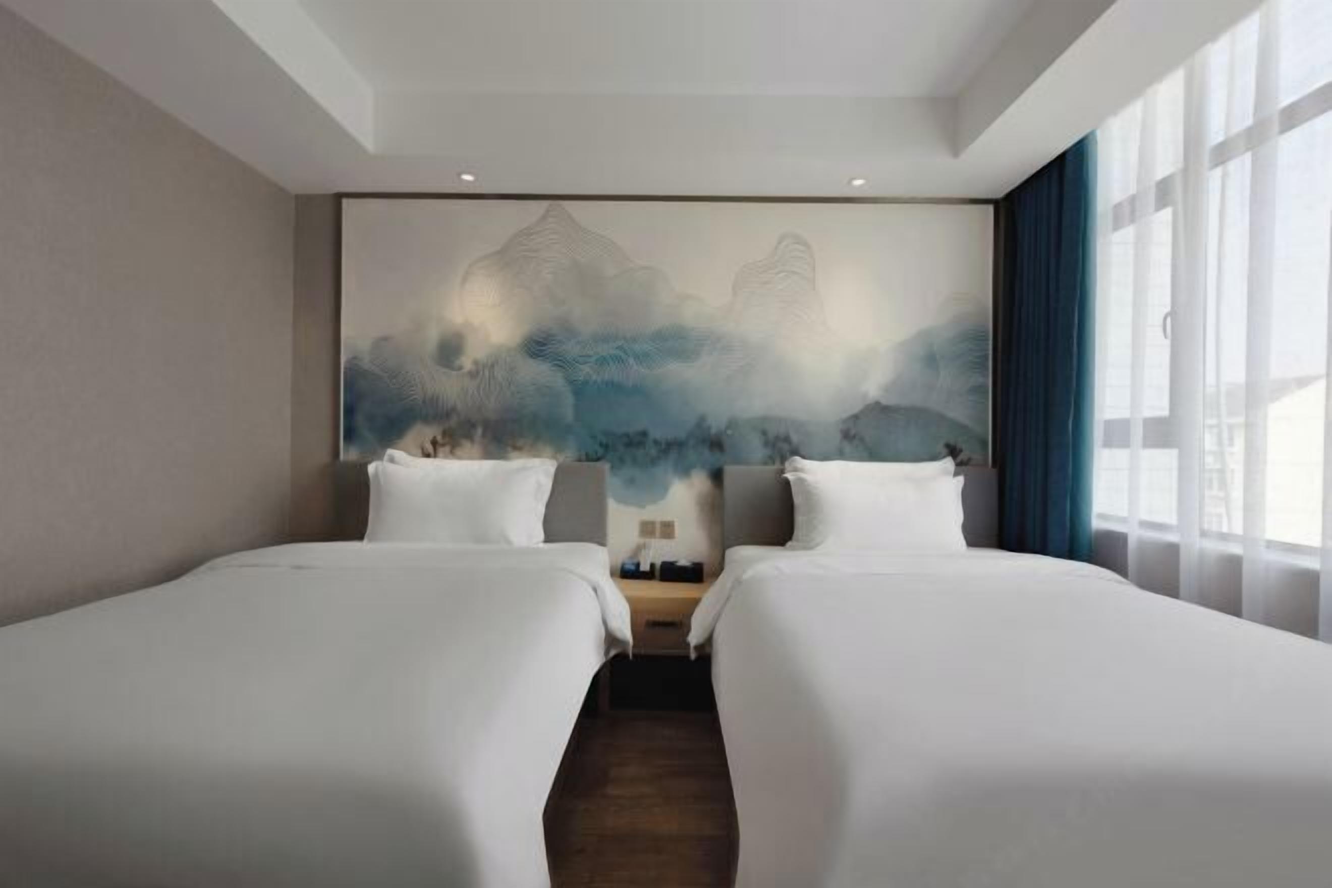 Quarto de hotel com duas camas, um grande mural na parede e uma janela com cortinas.