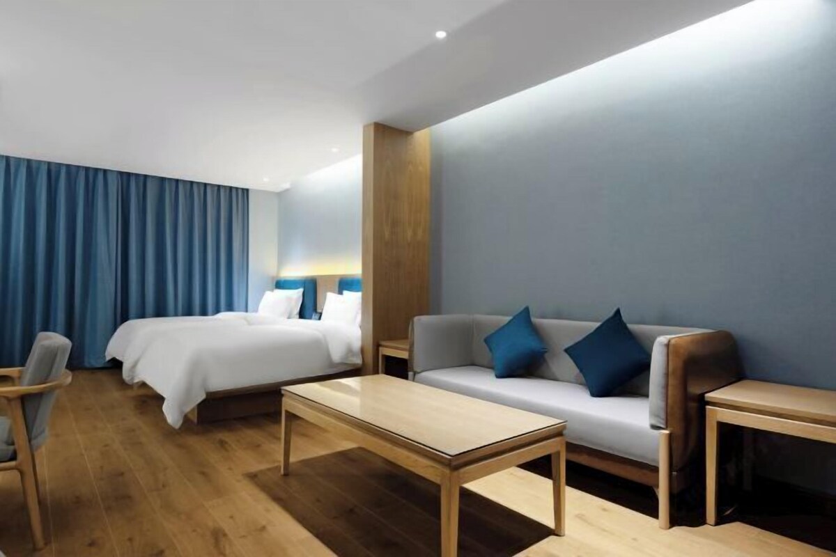 A modern hotel room with a bed, a sofa, a coffee table, and a chair.
