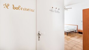 Une chambre avec un lit, une porte sur laquelle est apposée une pancarte indiquant la présence d’un balcon, et un ventilateur de plafond.