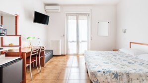 Une chambre d’hôtel comprenant un lit, un bureau avec une chaise, une télévision et une fenêtre avec des rideaux.