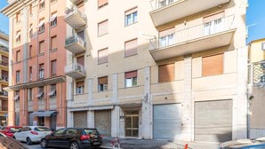 Un immeuble résidentiel à plusieurs étages, doté de balcons, d’une porte de garage et de voitures garées.