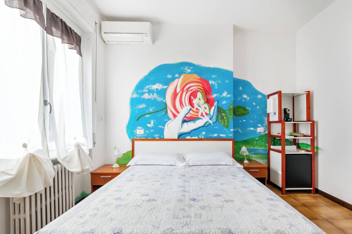 Een slaapkamer met een groot bed, een nachtkastje, een dressoir en een muurschildering.