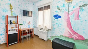Une pièce comprenant une table à manger, des chaises, un téléviseur fixé au mur, un radiateur et une grande fresque murale.