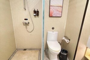 Un baño con ducha, inodoro y un cubo de basura.