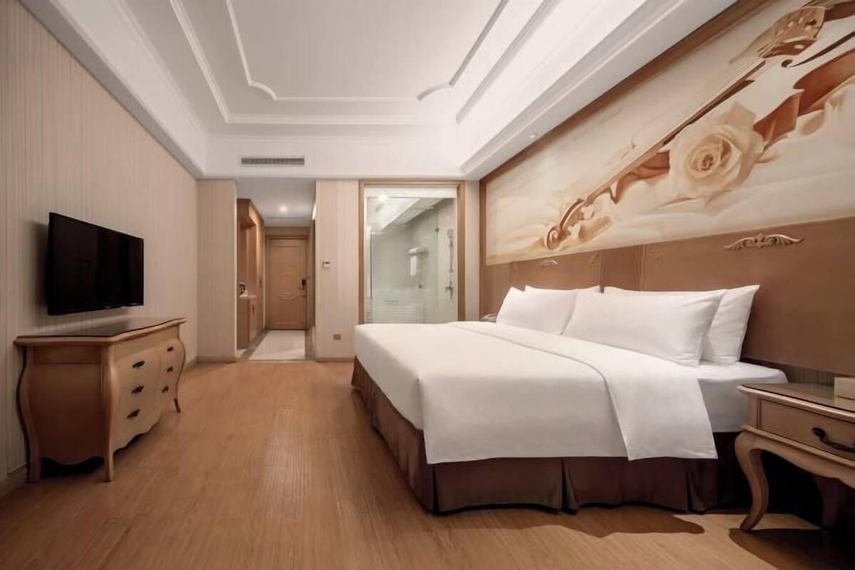 A hotel room with a bed, a television, a dresser, and a painting on the wall.
